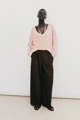 Pantalón de tiro alto y pernera ancha, color marrón, con pinzas delanteras, bolsillos frontales y cierre con cremallera y botón.