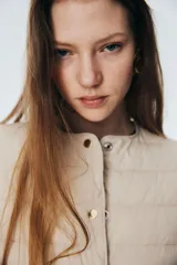 Campera acolchada de nylon color beige, con cuello redondo, cierre de botones a presión y bolsillos laterales discretos. Tiene elástico fino en los puños y está forrada.