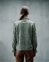 Camisa de lana a cuadros con diseño romántico. Presenta un canesú con bordado y frunces, cuello con volado y cierre frontal con botones de nácar. Las mangas son largas con puños elásticos fruncidos que terminan en un pequeño volado.