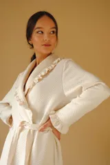 Bata larga color blanco, confeccionada en algodón capitoneado con diseño de espiga. Presenta volados en el cuello y puños, y lazo de ajuste en la cintura.