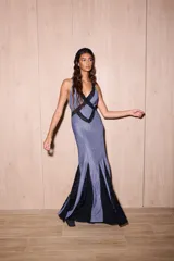 Vestido largo de silueta fluida, entallado en el torso, con escote profundo en V y espalda descubierta con tiras cruzadas. El cuerpo del vestido es de tejido jersey con lurex azul, y la falda presenta paneles triangulares de encaje negro con diseño de lunares.