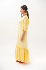 Vestido largo amarillo mantequilla con escote en V, mangas abullonadas y volados en el bajo con detalles de broderie.