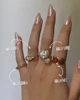 Set de cuatro anillos dorados de diferentes estilos: uno liso con bolitas, uno con textura trenzada, uno con una perla irregular y una piedra transparente, y uno con una piedra naranja facetada.