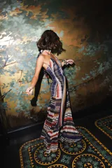 Vestido largo de encaje y transparencias color marrón, con escote profundo halter, frunces en el cuerpo, espalda abierta y tiras largas estampadas para atar al cuello.