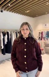 Cardigan de punto con diseño de trenzas, cuello redondo y cierre frontal con botones grandes a contraste. Posee puños y ruedo acanalados.