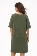 Vestido corto de corte recto y estilo minimalista, confeccionado en tela tipo gamuza negra. Presenta cuello redondo, mangas cortas y dos bolsillos frontales aplicados a la altura de la cadera.