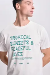 Remera blanca de manga corta con cuello redondo y estampado con la frase "Tropical Sunsets & Peaceful Waves" en color verde.