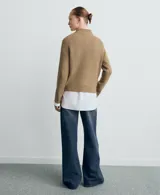 Sweater de punto color beige, con cuello alto y diseño de manga larga raglán con detalle de línea blanca lateral. Presenta un tejido acanalado y corte recto.