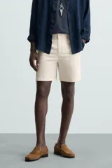 Bermuda de hombre color beige claro, corte regular fit, con pliegues frontales, bolsillos delanteros y bolsillos traseros de doble vivo con botón.