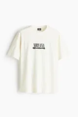 Remera color crema de corte holgado con estampado frontal del logo de la banda Nirvana y el título de su álbum Nevermind en color negro.