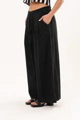 Pantalón negro de pierna súper amplia, confeccionado en denim fino y liviano con caída fluida. Tiene cintura elastizada con lazo regulable, bolsillos laterales y pinzas en la delantera.