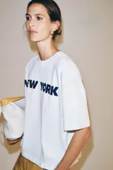 Remera oversize blanca de algodón con cuello redondo, manga corta y estampa con la inscripción 'NEW YORK' en color negro en el frente.