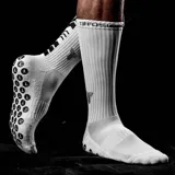 Medias deportivas de caña media color negro, con diseño técnico que incluye zonas de compresión y puntos de silicona antideslizantes en la planta del pie para mayor agarre. Presenta el logo de la marca en el lateral.