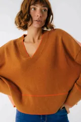Sweater de punto color marrón con detalles en naranja neón en el cuello en V, puños y ruedo. De diseño holgado y manga larga.
