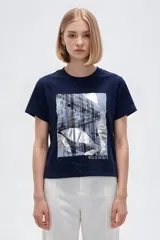 Remera de manga corta de algodón en color blanco, con cuello redondo y diseño holgado. Presenta un estampado frontal con detalle de acabado metálico (foil).