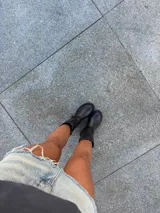 Bota biker de caña media confeccionada en cuero vacuno encerado. Presenta un diseño robusto con hebillas metálicas niqueladas en la caña y en la zona del tobillo, con una argolla decorativa. Cuenta con suela de goma negra con plataforma y cierre lateral interno.