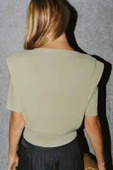 Top de punto color verde claro con cuello redondo, manga corta, hombreras marcadas y pliegues decorativos en la parte frontal.