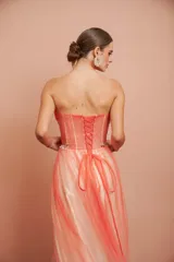 Vestido largo de fiesta, strapless, con busto drapeado y falda de tul con degradé de color coral a blanco. Presenta bordados florales en el corpiño.