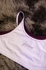 Top deportivo de entrenamiento con doble capa, color blanco exterior y borgoña interior. Presenta un corte de tirantes anchos y el logo "Hermod" en cursiva color borgoña en el pecho.