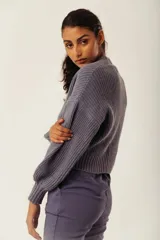 Saco de tejido de punto grueso color gris azulado, con cuello en V y manga larga abullonada. Presenta un solo botón de madera en la parte inferior delantera.