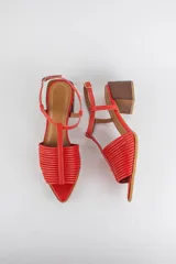 Sandalias de cuero rojo con diseño de tiras horizontales abullonadas en la parte delantera, punta fina, tira vertical central en forma de T y tira ajustable al tobillo. Poseen tacón cuadrado de madera de 6 cm.