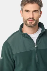 Buzo de micro polar con interior térmico, cuello alto y cierre frontal parcial. Presenta paneles de taslón al tono en el frente y cuello, con bolsillos laterales con cierre y detalle de logo en la manga.