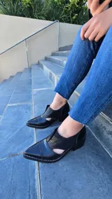 Zapatos de cuero color tostado con puntera fina y tacón bajo, estilo botineta destalonada con laterales abiertos y paneles elásticos en el empeine.