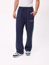 Pantalón tipo babucha de la marca Rusty, color azul marino con franjas laterales en verde y blanco. Presenta cintura elástica con cordón ajustable y logo de la marca bordado en el frente.