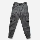 Pantalón cargo negro de corte relajado, con cintura elástica ajustable con cordón, bolsillos laterales con solapa y botones, y puños elásticos en los tobillos.