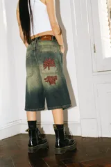 Bermuda de jean estilo baggy con lavado verde desgastado. Presenta grandes bolsillos traseros con bordados en hilo rojo que simulan caracteres chinos.