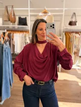 Blusa de color bordó con cuello drapeado y detalle de cinta tipo choker integrada. Presenta mangas largas con puños abotonados y un corte holgado y fluido.