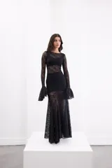 Vestido largo de encaje negro con transparencias, corte ajustado al cuerpo, mangas largas con terminación acampanada y falda con caída fluida.