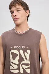 Musculosa oversize de algodón color marrón con efecto lavado desgastado, de corte amplio y sin mangas. Cuenta con una estampa frontal en relieve y diseño urbano de la marca Mistral.