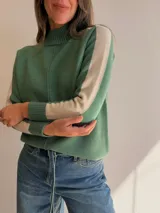Sweater de tejido de punto en color verde con detalles en beige en las mangas. Presenta cuello alto, costura central vertical y diseño de mangas ranglan con franjas laterales en contraste.