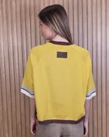 Buzo de punto color tostado, con mangas cortas holgadas y detalles de franjas en negro, blanco y beige en el cuello, los puños y el ruedo.