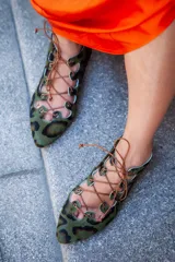Semibotín de piel de pony con estampado animal print en tonos verde y marrón. Presenta un diseño con aberturas laterales onduladas, cierre de cordones finos y punta afilada. Cuenta con suela de cuero y cuña interna.