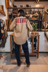 Sobre camisa beige de manga larga, con bolsillos en el pecho y detalles de tela guardamonte en los bolsillos y puños.