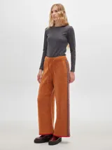 Pantalón ancho y suelto de tejido tipo terciopelo color naranja, con cintura elástica y cordón ajustable. Presenta detalles de pespuntes decorativos a los lados.