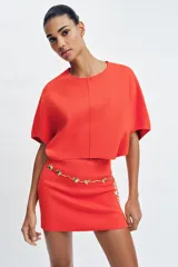 Top corto de punto color rojo coral, con cuello redondo y mangas cortas amplias con sisa ancha y costura central vertical.