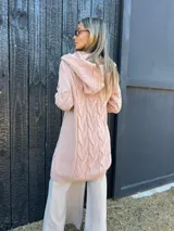 Saco tejido de punto color rosa, con diseño de trenzas, capucha y frente abierto.