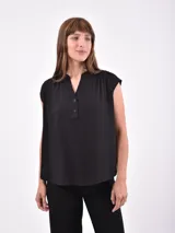 Blusa negra sin mangas, con cuello mao y abertura frontal con botones. Presenta frunces en la zona de los hombros, dándole un calce holgado.