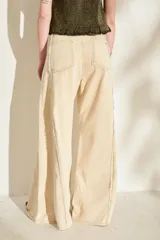 Jeans de corte wide leg, tiro alto y color beige, con detalles de costuras desflecadas a lo largo de las piernas.
