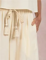Pantalón palazzo de tiro alto marca Elan, en color beige, confeccionado en mezcla de algodón, viscosa y lino. Presenta cintura delantera plana con parte trasera elastizada, bolsillos laterales funcionales y corte de pierna ancha. Incluye un cinturón trenzado al tono con terminación en borlas y flecos.