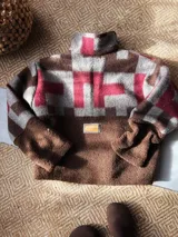Buzo de abrigo con diseño de bloques, confeccionado en una combinación de corderito marrón y textiles vintage con estampado a cuadros en tonos gris, marrón y bordó. Presenta cuello alto con cierre frontal parcial y mangas largas.