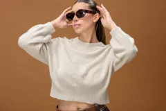 Sweater de punto fino color beige, con cuello redondo, mangas largas y diseño corto con terminación acanalada en la cintura.