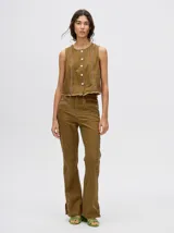 Pantalón de denim color marrón, de tiro alto y calce ochentoso con terminación estilo oxford. Cuenta con apliques metálicos decorativos alrededor de los bolsillos y a lo largo de las costuras exteriores.