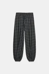Pantalón bombacho de tiro medio con estampado a cuadros en tonos oscuros (negro, gris, blanco). Presenta cintura elástica ajustable con cordones y bajo abullonado con elástico.