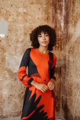 Vestido midi de jersey color naranja con estampado abstracto en negro. Tiene mangas largas abullonadas y escote redondo.