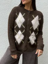 Cárdigan de punto con textura suave y efecto peluche, color marrón con diseño de rombos en tonos claros y líneas amarillas. Presenta cierre frontal con botones y cuello redondo.