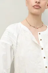 Vestido corto negro con bordado floral blanco, escote redondo con abotonadura frontal y mangas 3/4 abullonadas con pliegues en los hombros.